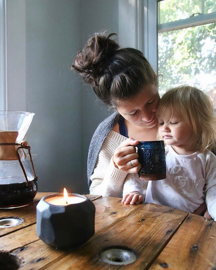 Mom and daughter share morning snuggles next to coffee and growing candle